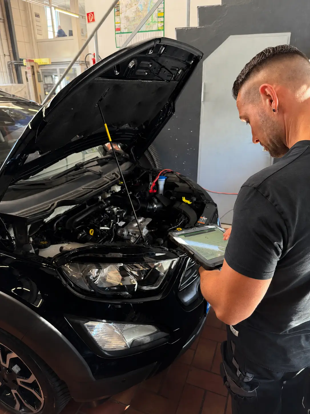 Fahrzeugdiagnose in Magdeburg: ein Mechaniker liest mit dem Diagnosetablet den Fehlerspeicher eines Autos mit geöffneter Motorhaube aus.
