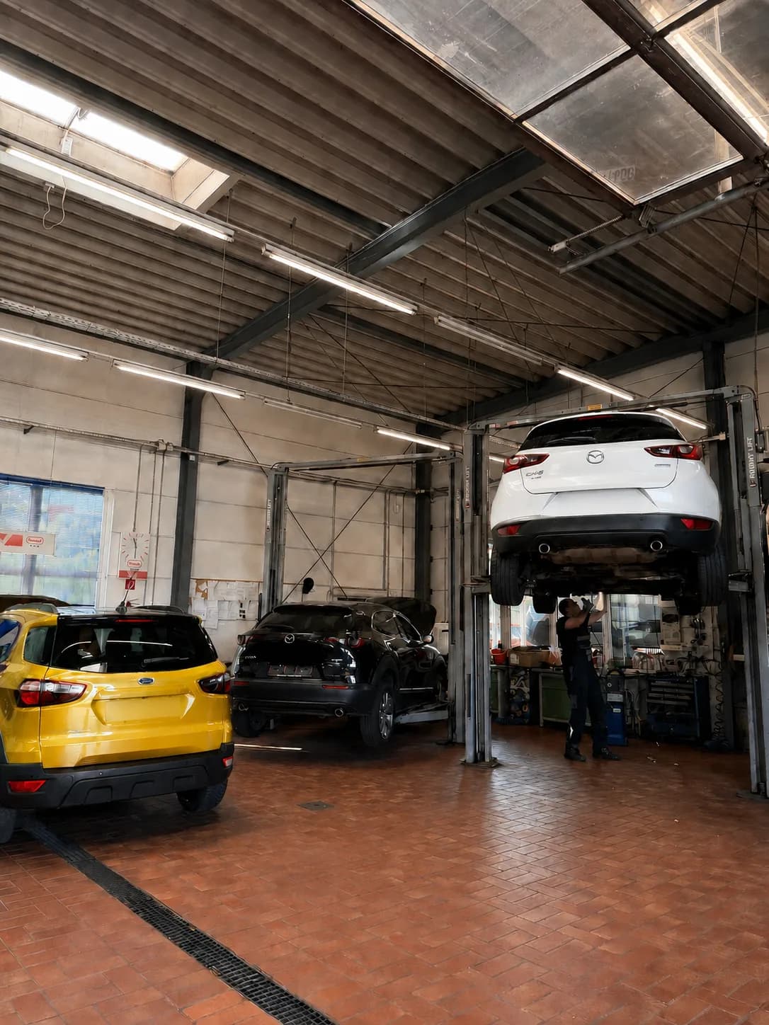 Autowerkstatt in Magdeburg: ein weißer Mazda steht auf der Hebebühne, ein Mechaniker arbeitet darunter, daneben zwei weitere Fahrzeuge in der Halle.