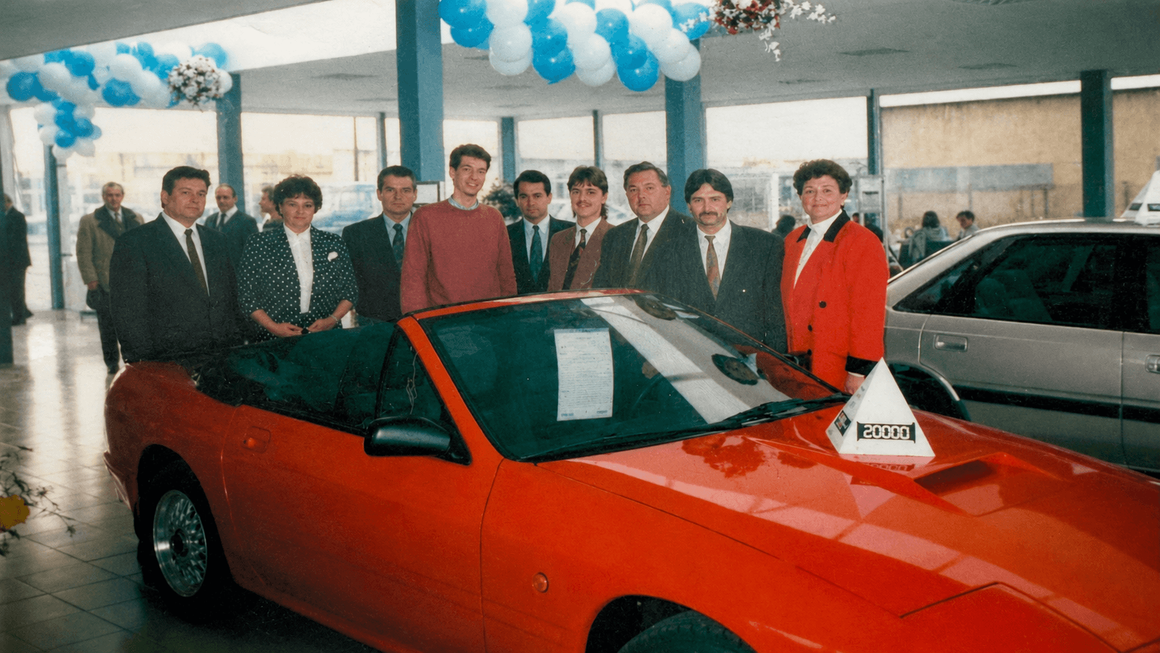 Belegschaft bei der Eröffnung im Ausstellungsraum, davor ein roter Mazda