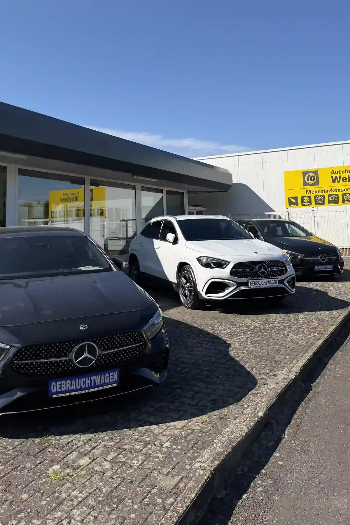 Gebrauchtwagen auf dem Hof, im Hintergrund die Halle mit dem Schild Autohaus Weber