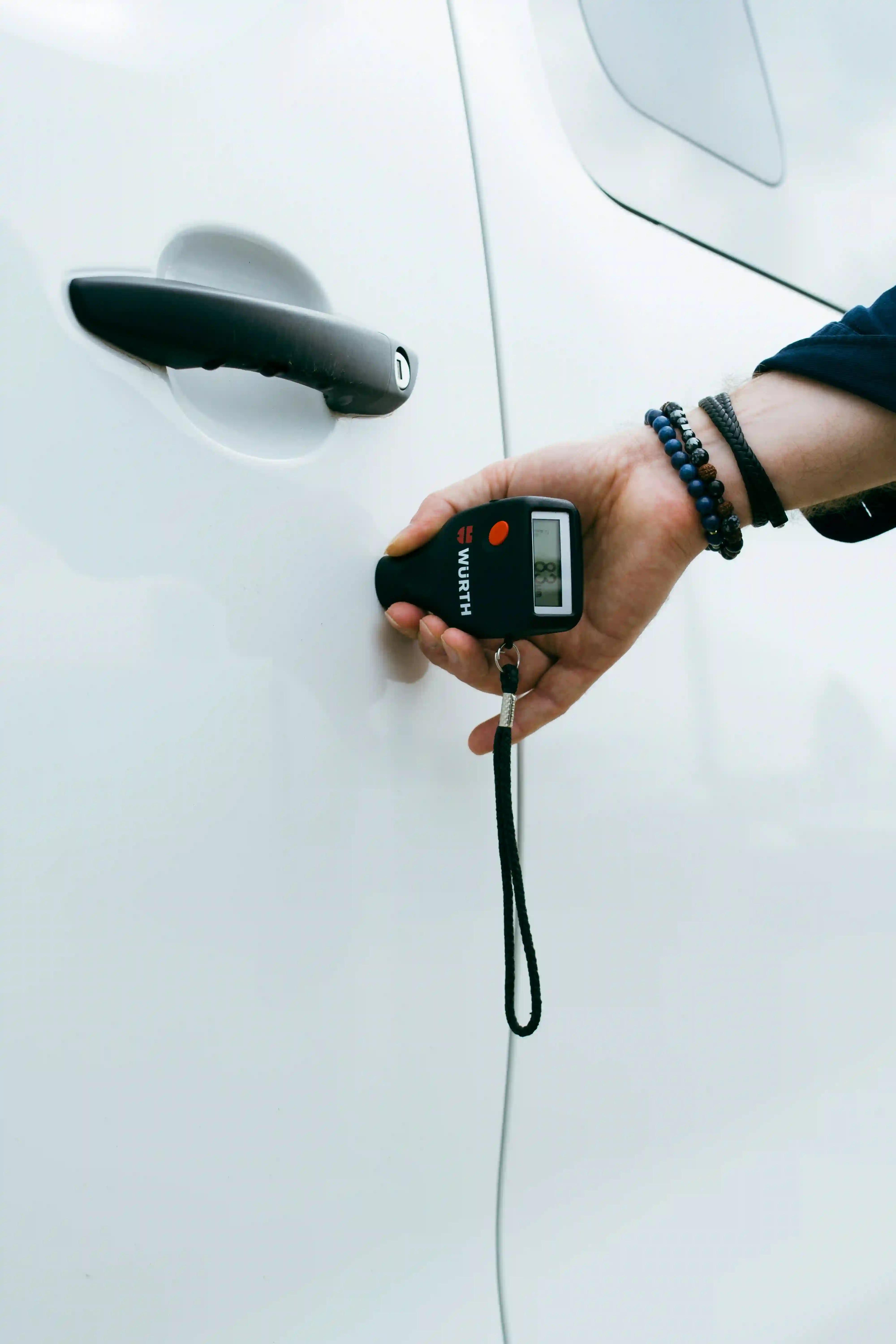 Lackschichtdicke messen: eine Hand hält ein Messgerät an die Tür eines weißen Autos.