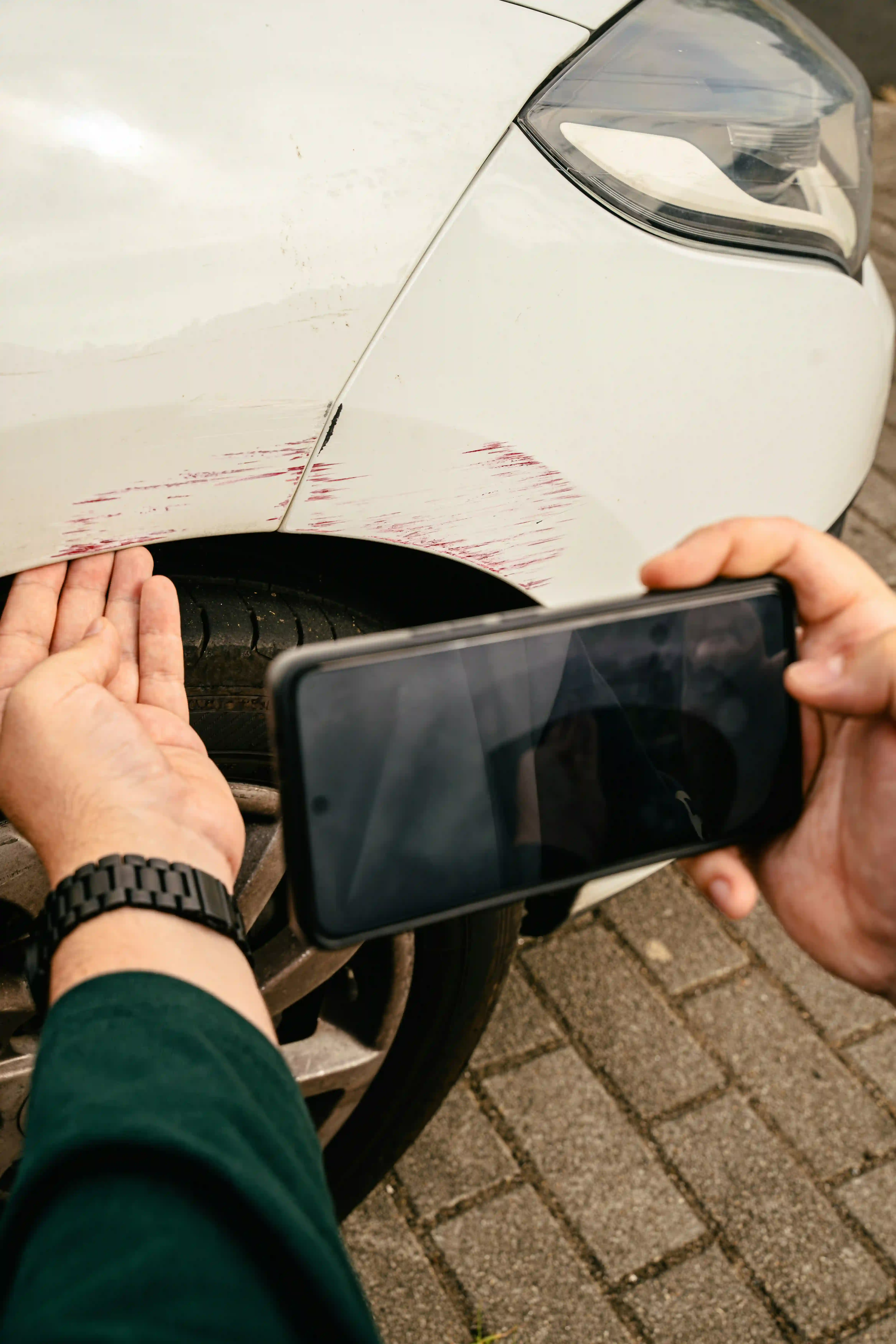 Schaden dokumentieren: zwei Hände fotografieren mit dem Handy einen Streifschaden am Kotflügel eines weißen Autos.